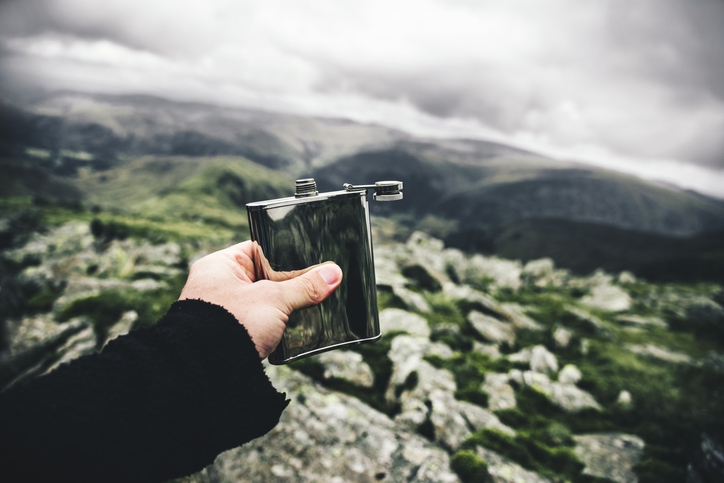 Holding a drinking flask out over a mountain range